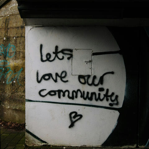 photo by mike erskine (creative commons license) black graffiti on a white wall reads "lets love our community" with a small heart shape beneath the words.